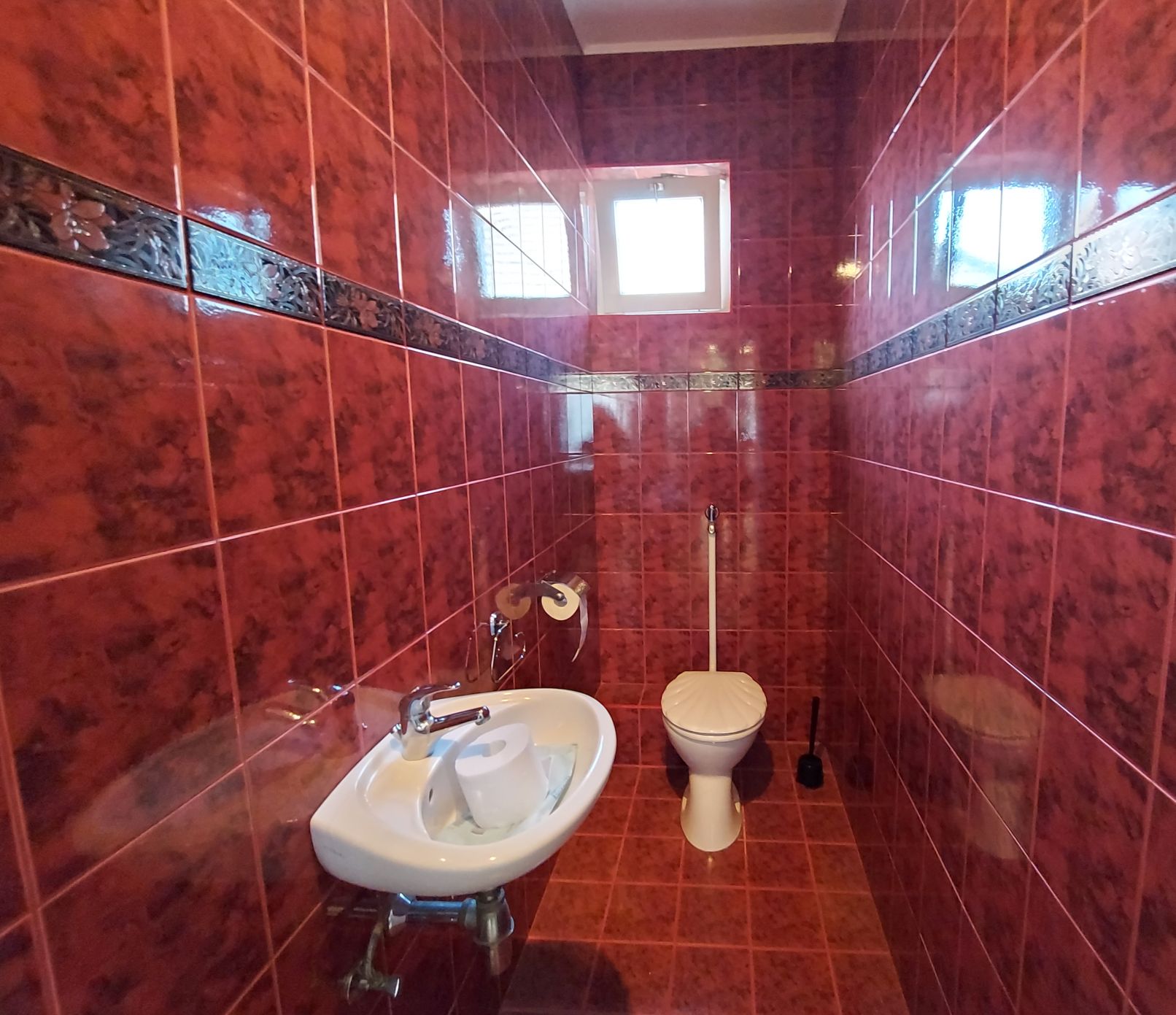 Rotes gefliestes Badezimmer mit Waschbecken, Toilette, Spiegeln und Deckenfenster, 