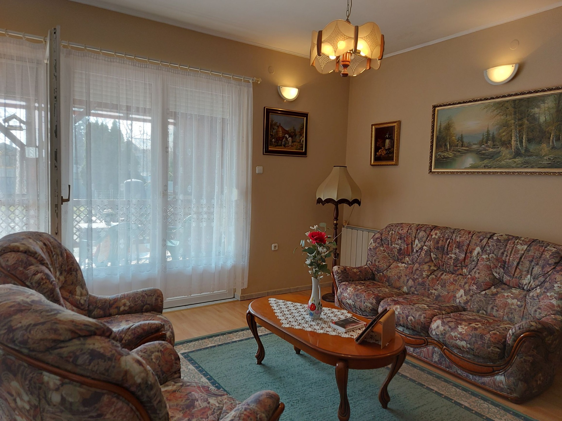Wohnzimmer mit gemusterten Sofas, Couchtisch, großem Fenster und goldener Deckenlampe.