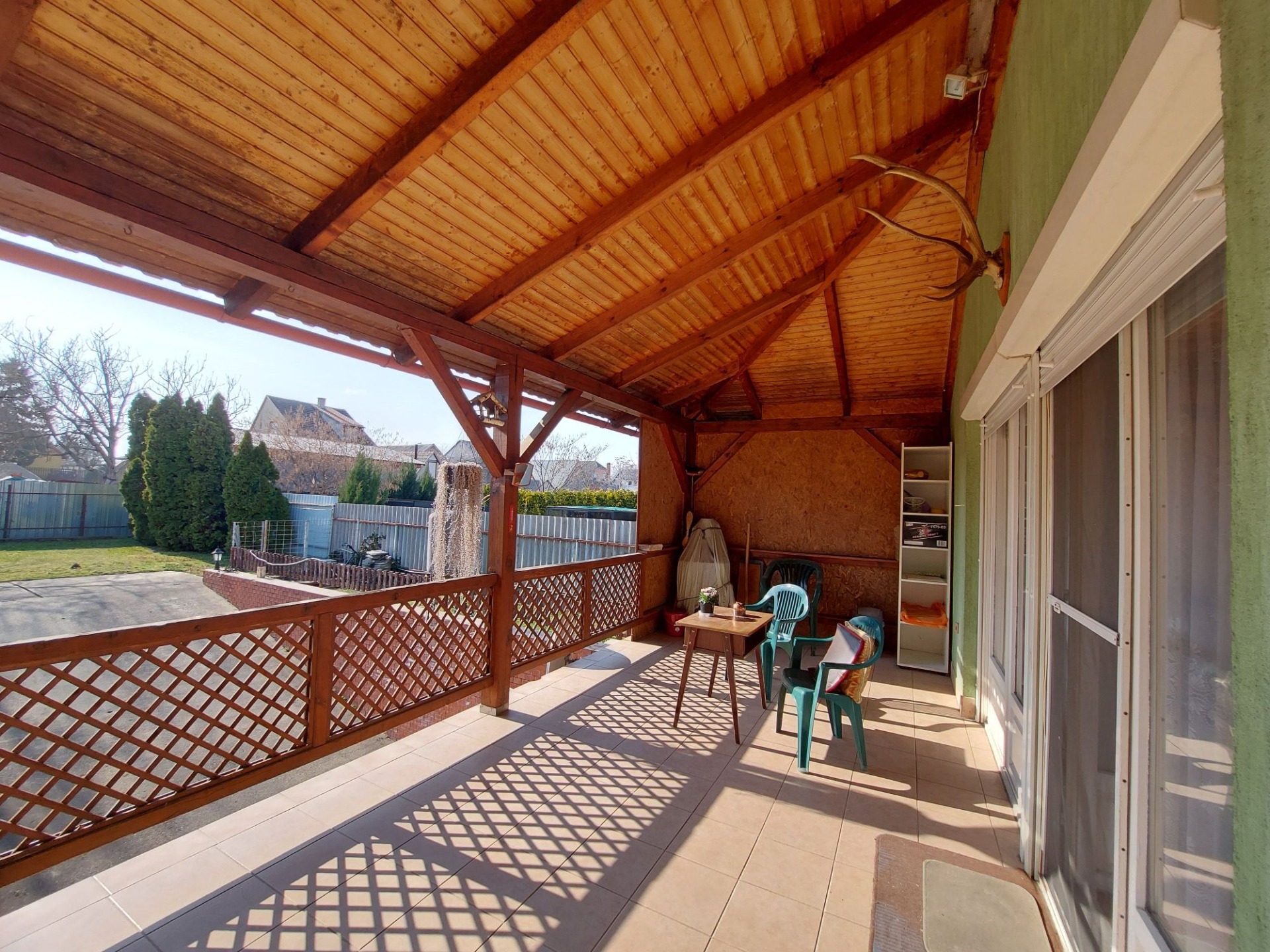 Überdachte Holzterrasse mit Geländer, Tisch und Stühlen, offenen Schiebetüren und Blick in den Garten.